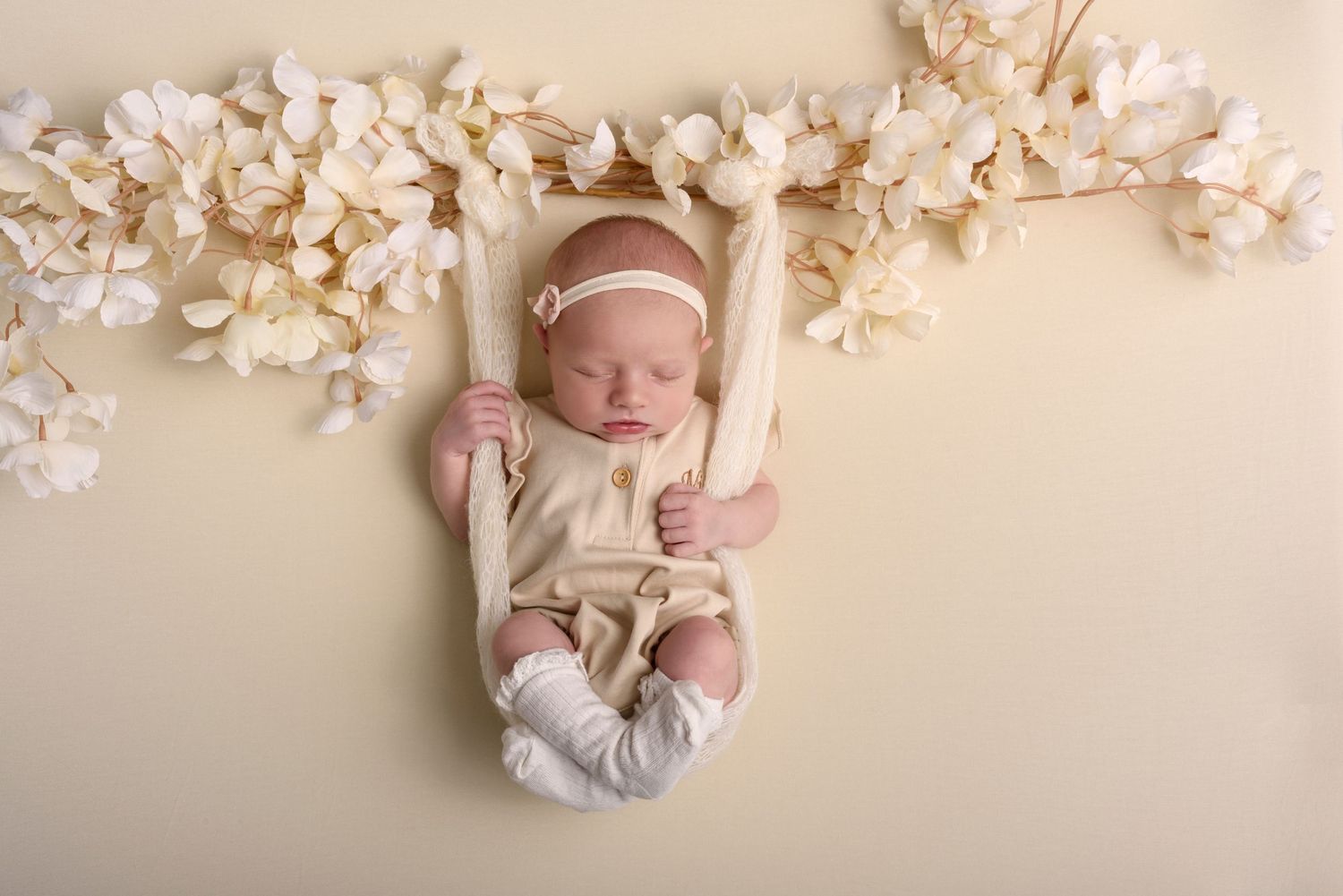Neutral beige backdrop with flower decorations creates soft newborn scene.