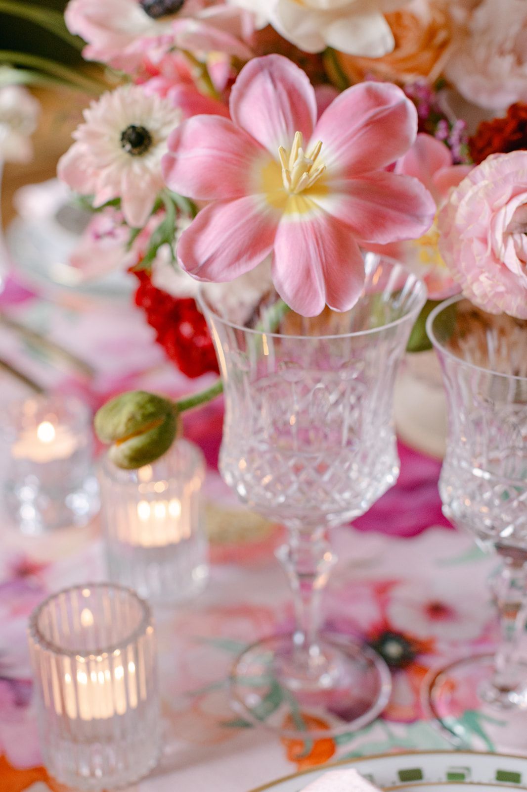 Elegant banquet hall with wood paneling, crystal chandeliers, and tables set with pink floral linens along a curved wall.