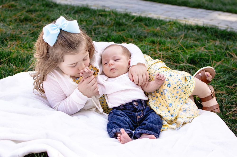 a little girl kissing the hand of a baby while laying on a blanket
