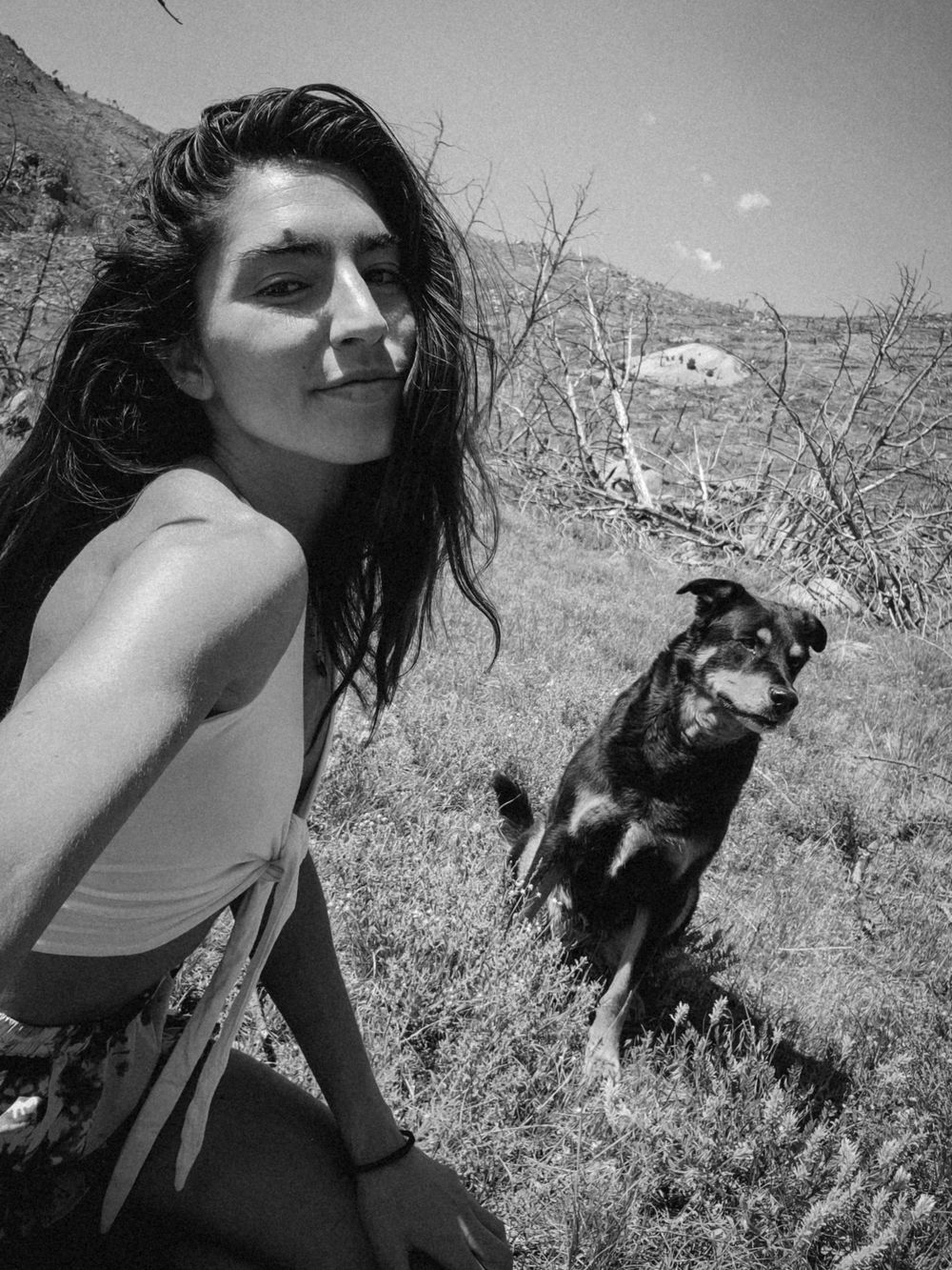 Black and white photo showing someone with a dog outdoors in a mountainous desert landscape.