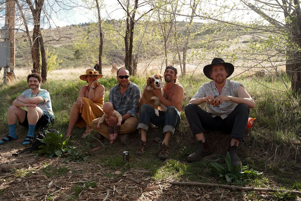 Group of people resting in the shade under trees on a sunny hillside during an outdoor adventure.