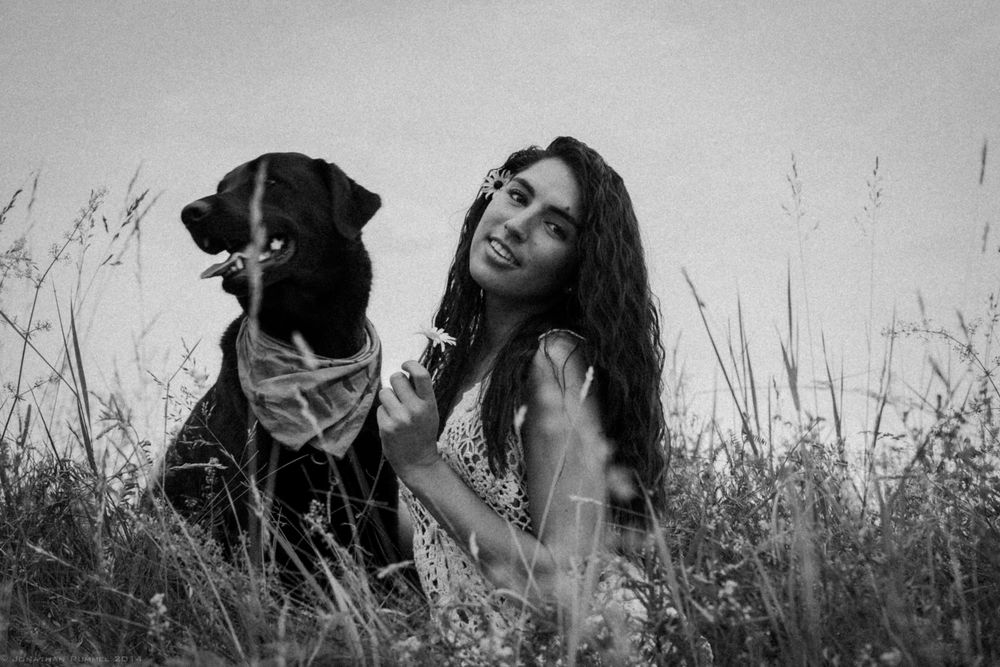 A black Labrador and someone sharing a candid moment together in tall grass, captured in black and white.