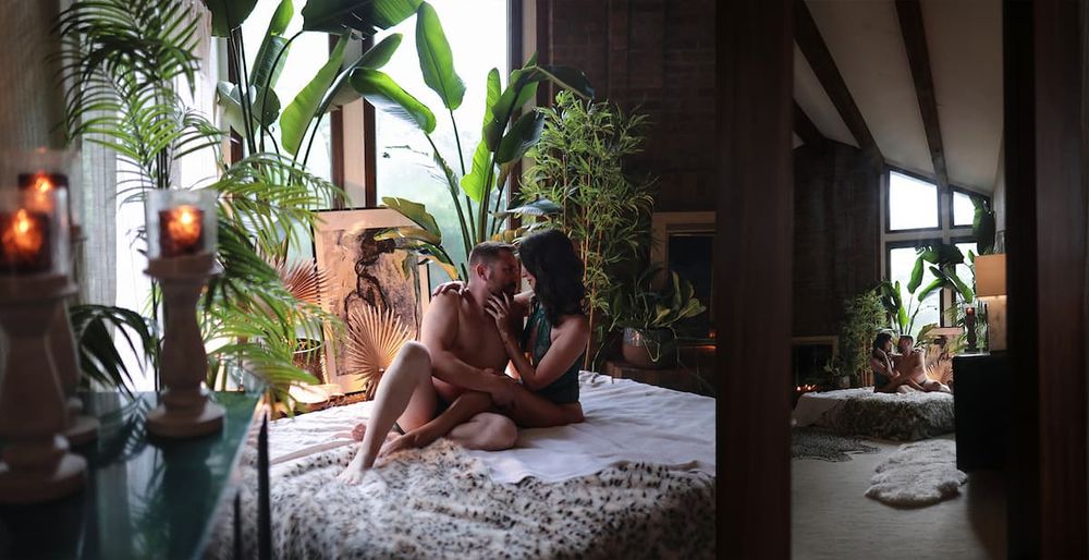Intimate bedroom scene with natural lighting filtered through indoor plants and candles.