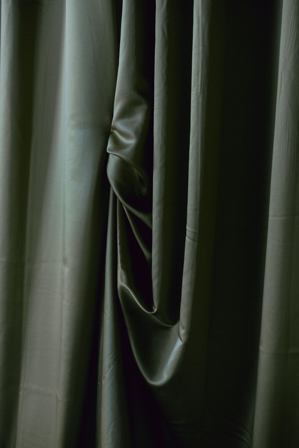 Closeup detail of green fabric curtain folds creating subtle shadows and texture.