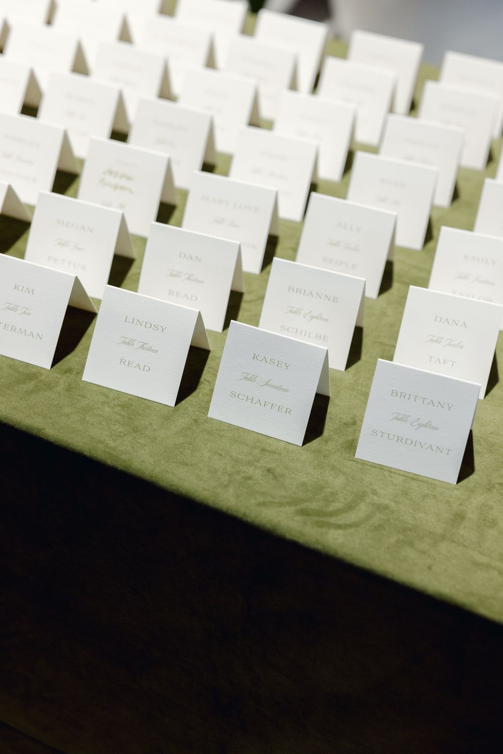 Rows of white place cards displayed on a green velvet surface for event seating.