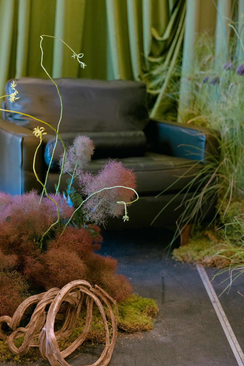 Whimsical floral installation with delicate blue flowers, pink smoke-like textures, and natural rope elements against green draping.