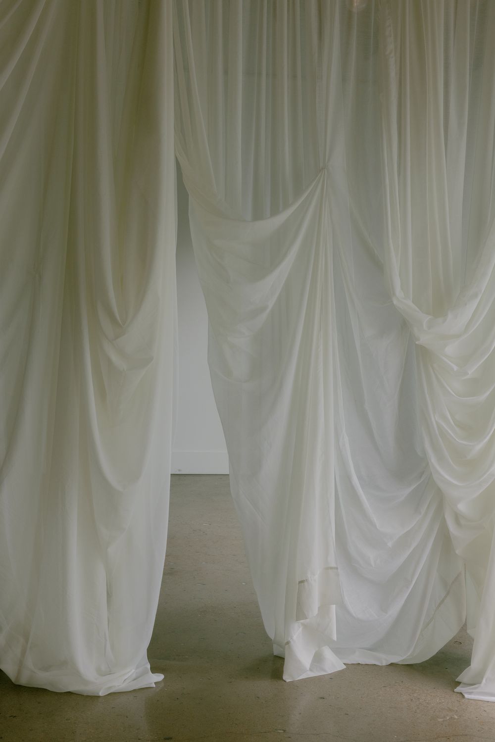 Elegant white draped curtains creating a soft, ethereal passage in an indoor space.