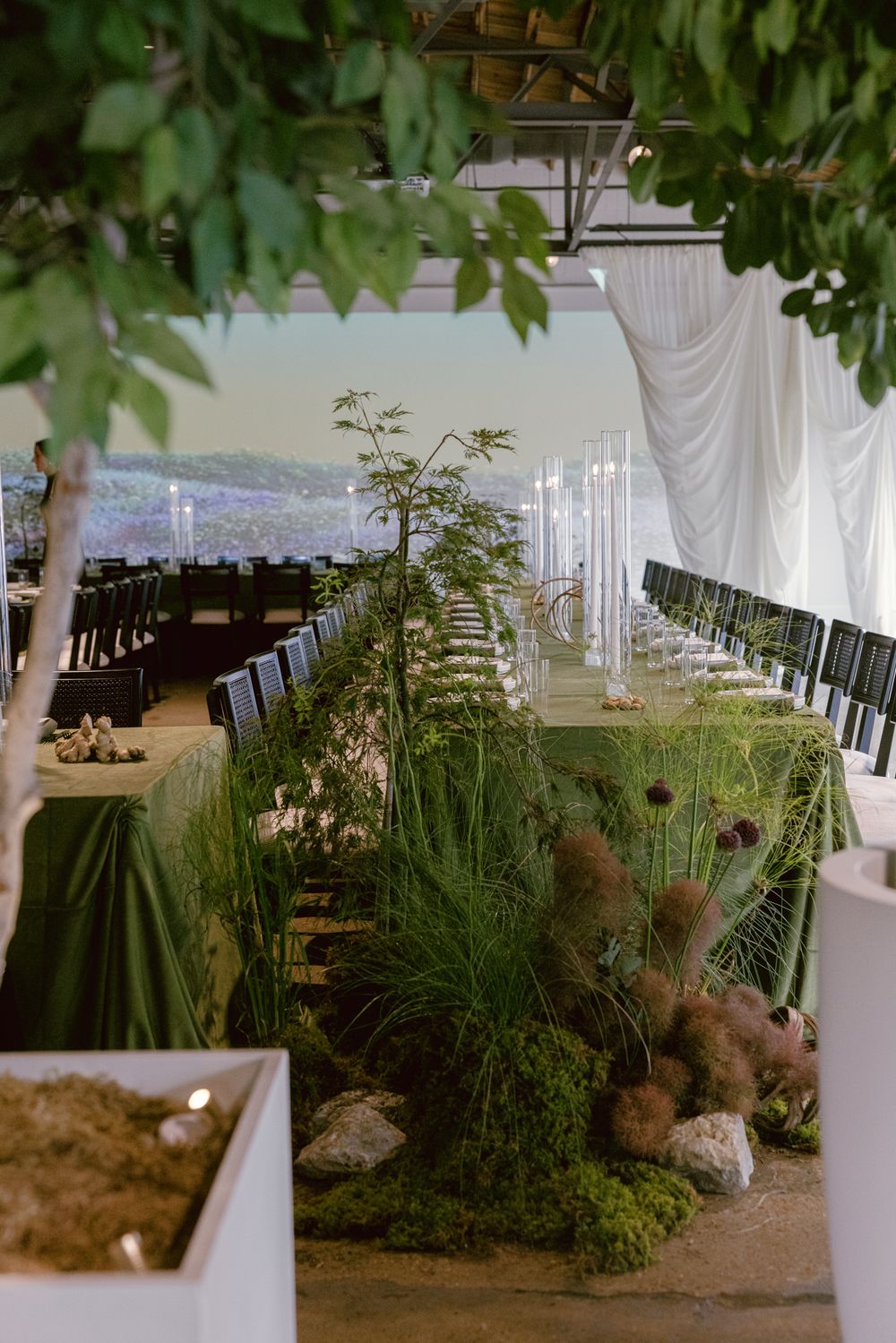 Modern wedding reception tent features natural tablescape with lush grasses, ferns and organic decor alongside mountain views.