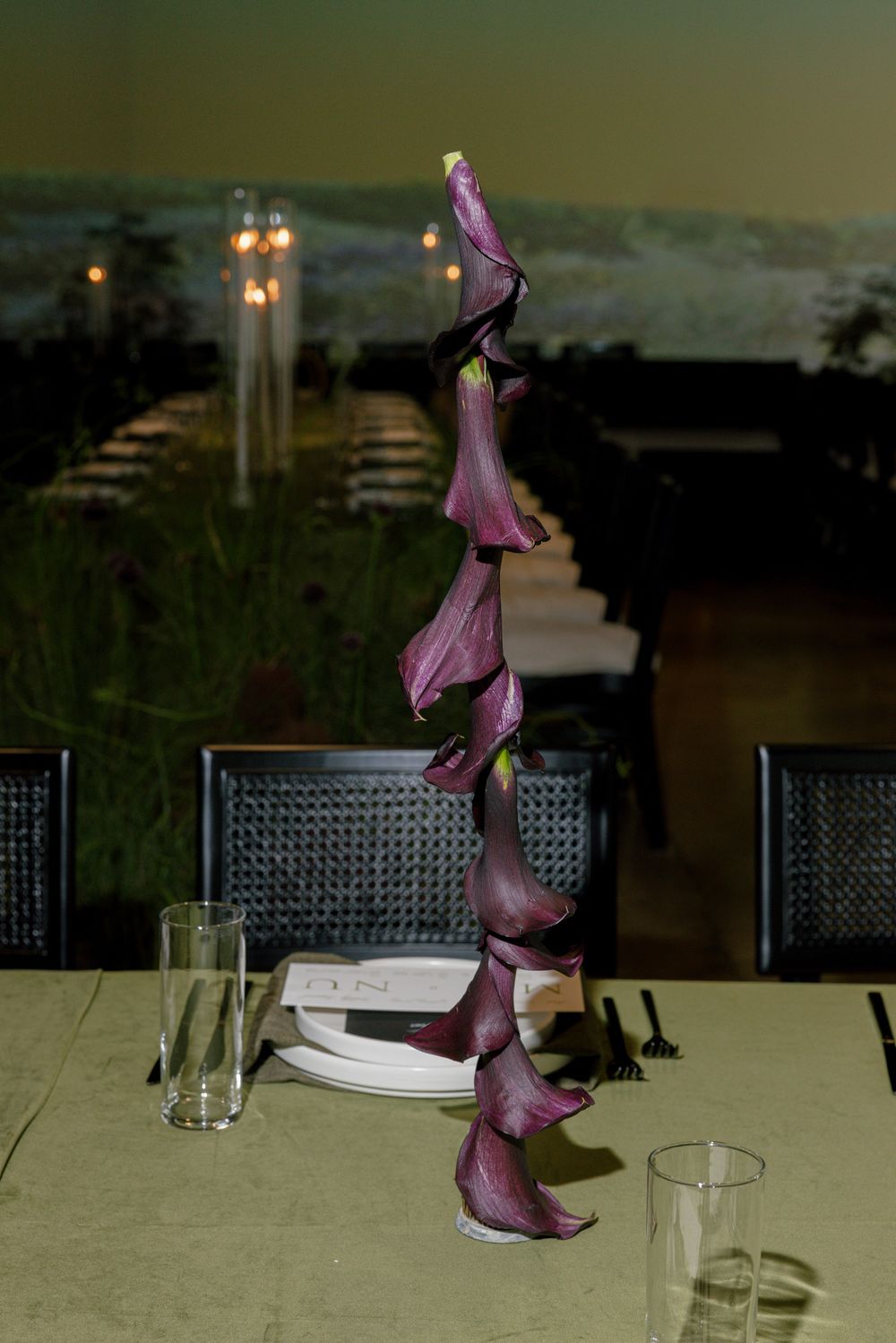 Purple floral sculpture centerpiece on dining table with glassware at dusk.