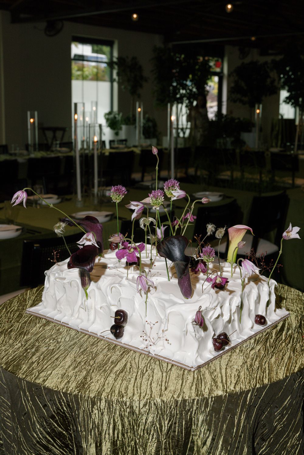 Elegant table setting with purple flowers and white napkins on textured gold tablecloth.
