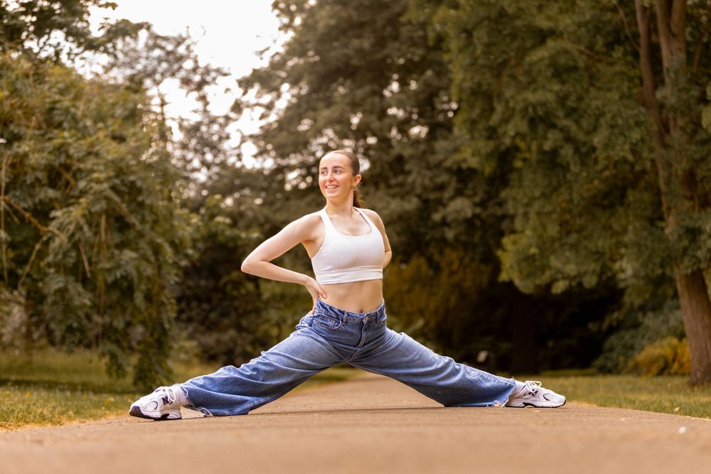 Person in athletic wear performing stretching exercises outdoors in a park-like setting.