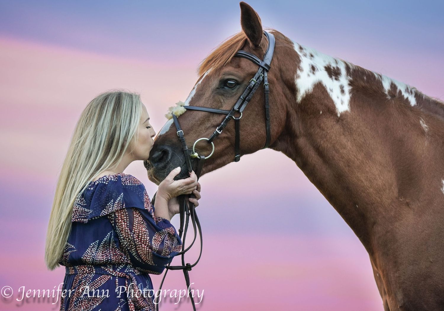 Paint horse and person share tender moment against pink sunset sky.