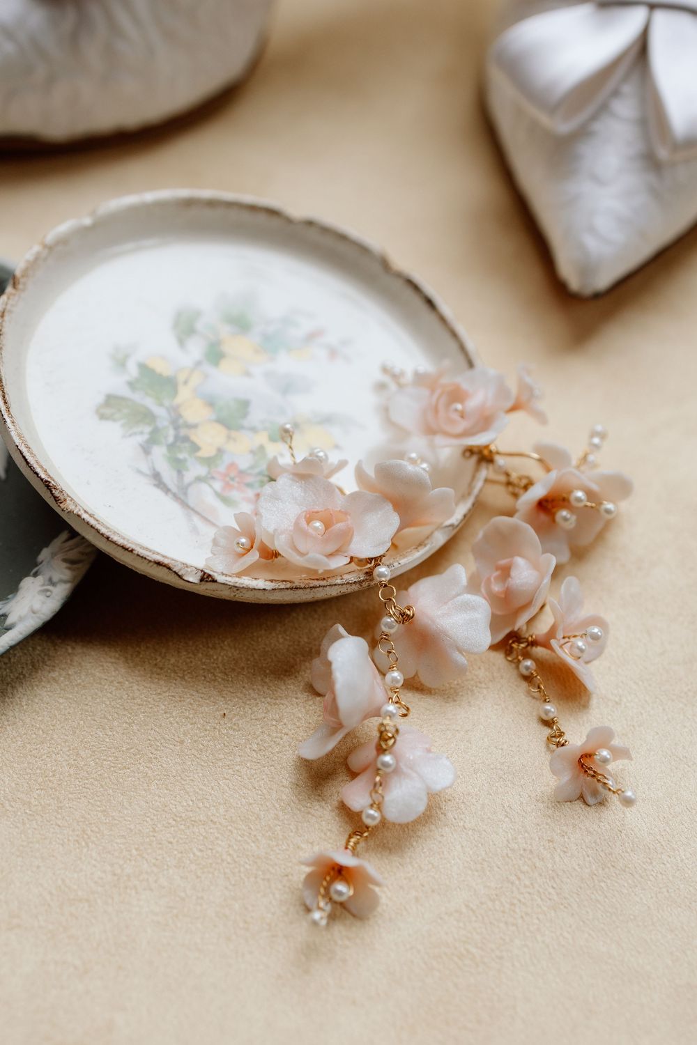 Delicate pink floral earrings with pearl accents resting on a vintage plate with floral design.