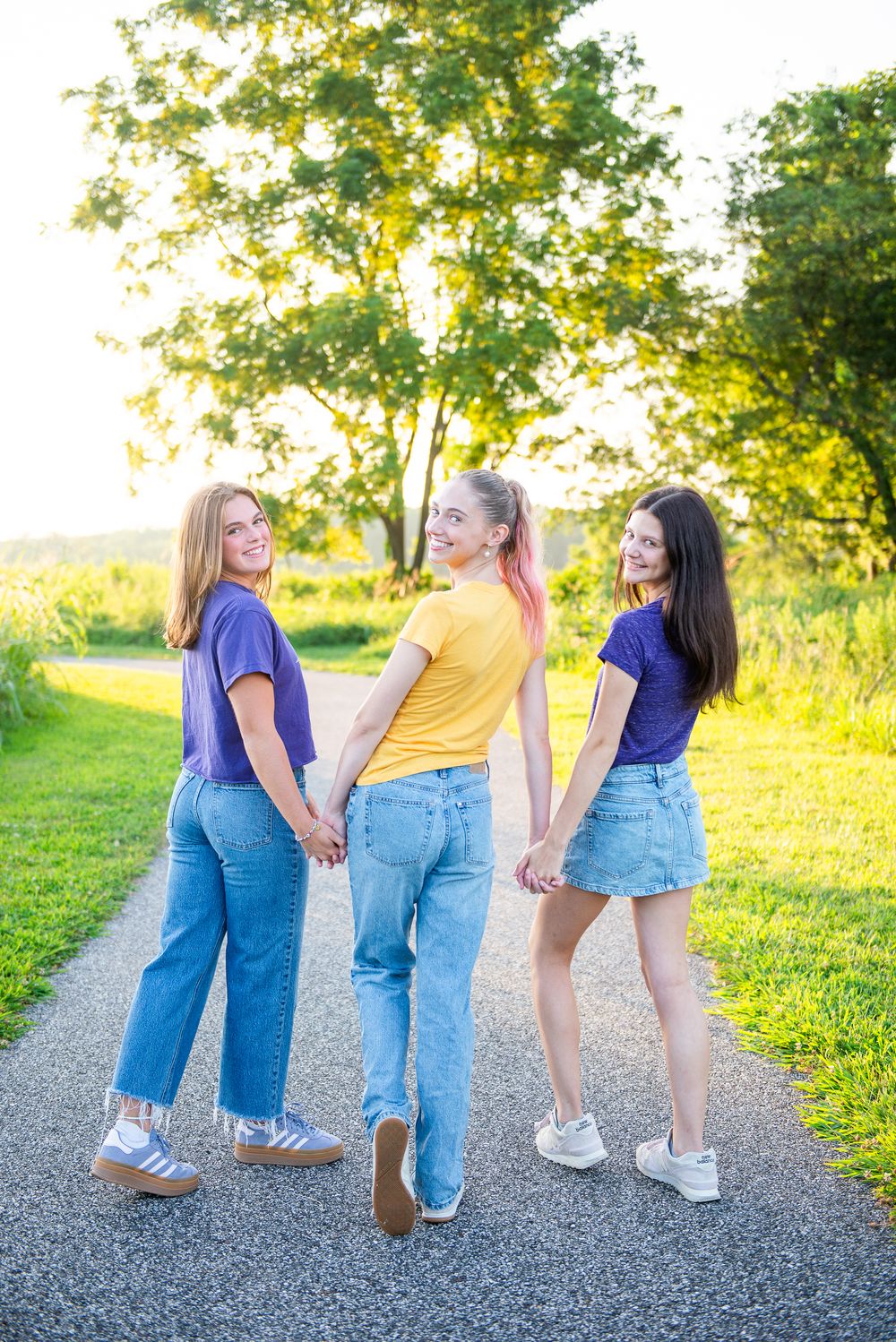 Three friends walking together on a sunny path wearing casual outfits of jeans and t-shirts in summer weather.