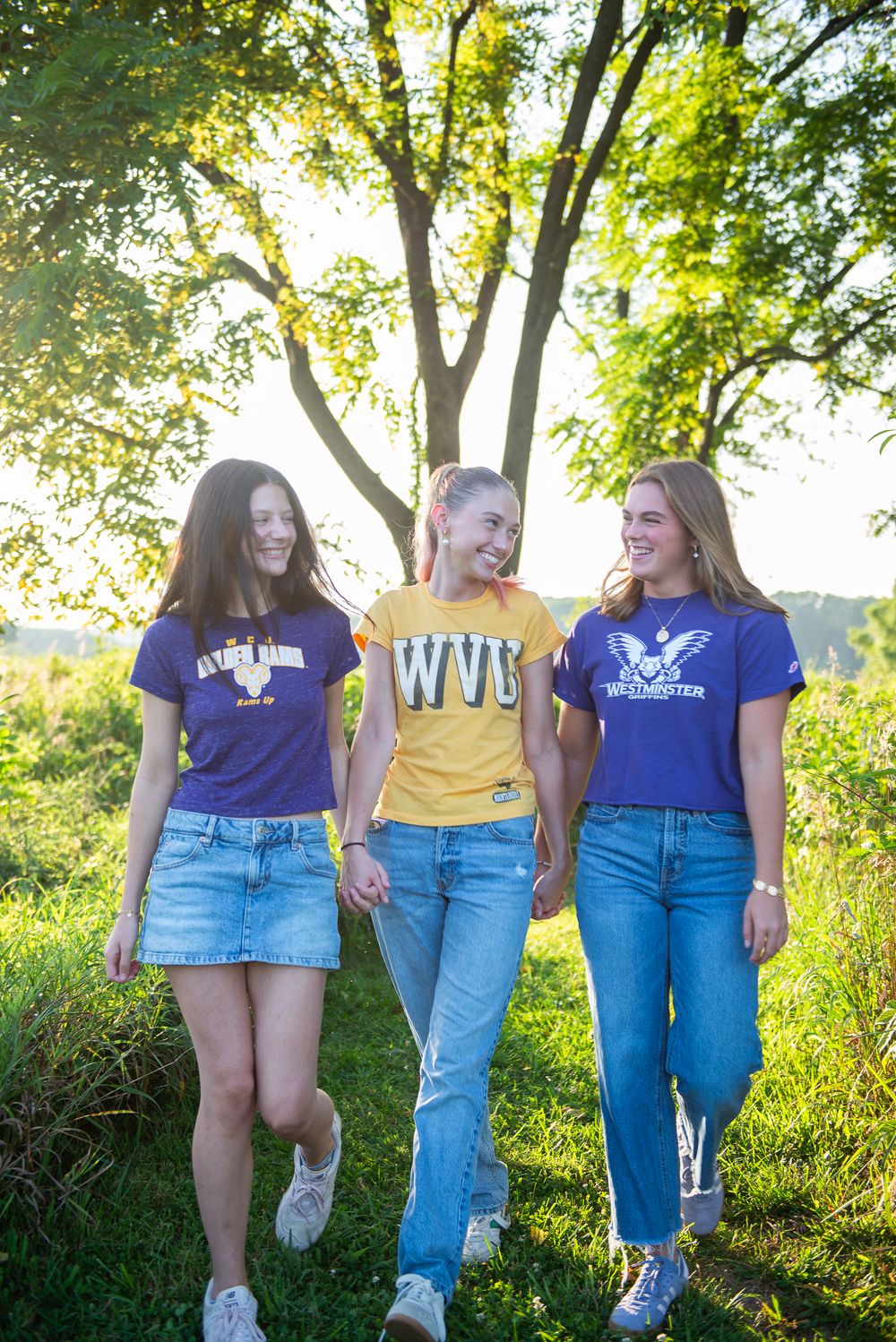 Three friends in coordinating purple and yellow t-shirts walk together on a sunny path.