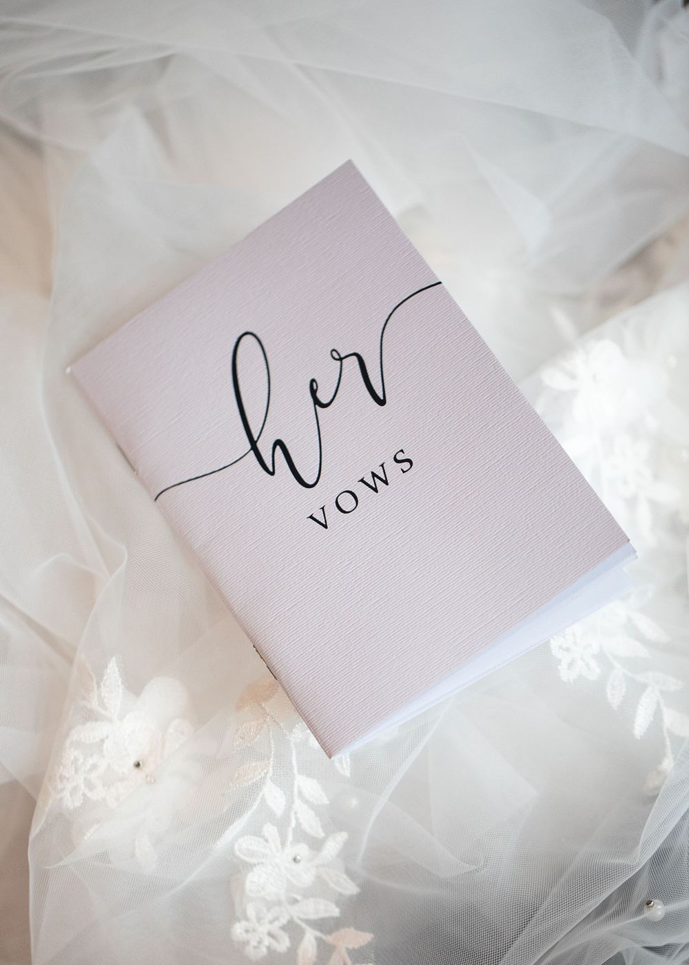 Elegant white wedding vow booklet with cursive script resting on delicate lace bridal veil.