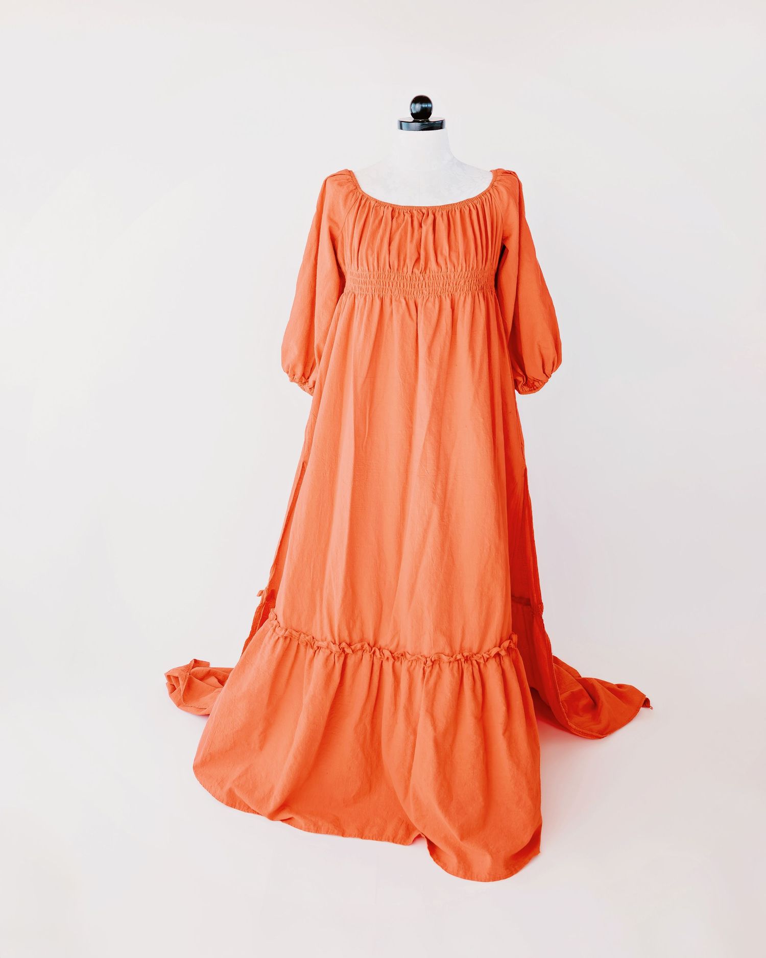 A vintage-inspired lace wedding dress with empire waist and flowy train displayed on a cream mannequin form.