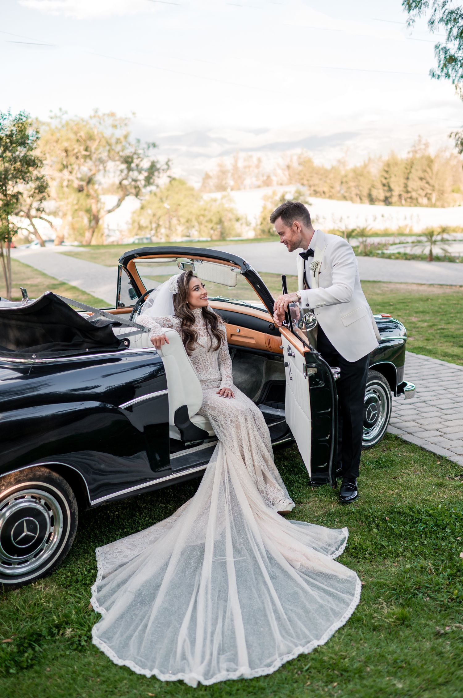 A classic black Mercedes convertible serves as an elegant backdrop for wedding photos.