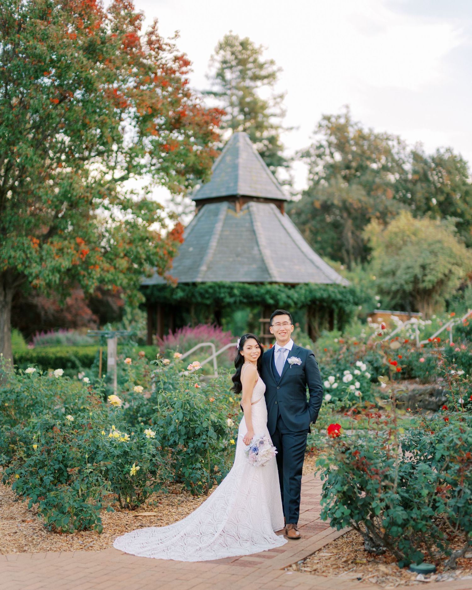 Wedding moment captured in a garden setting with a rustic gazebo backdrop surrounded by autumn foliage.