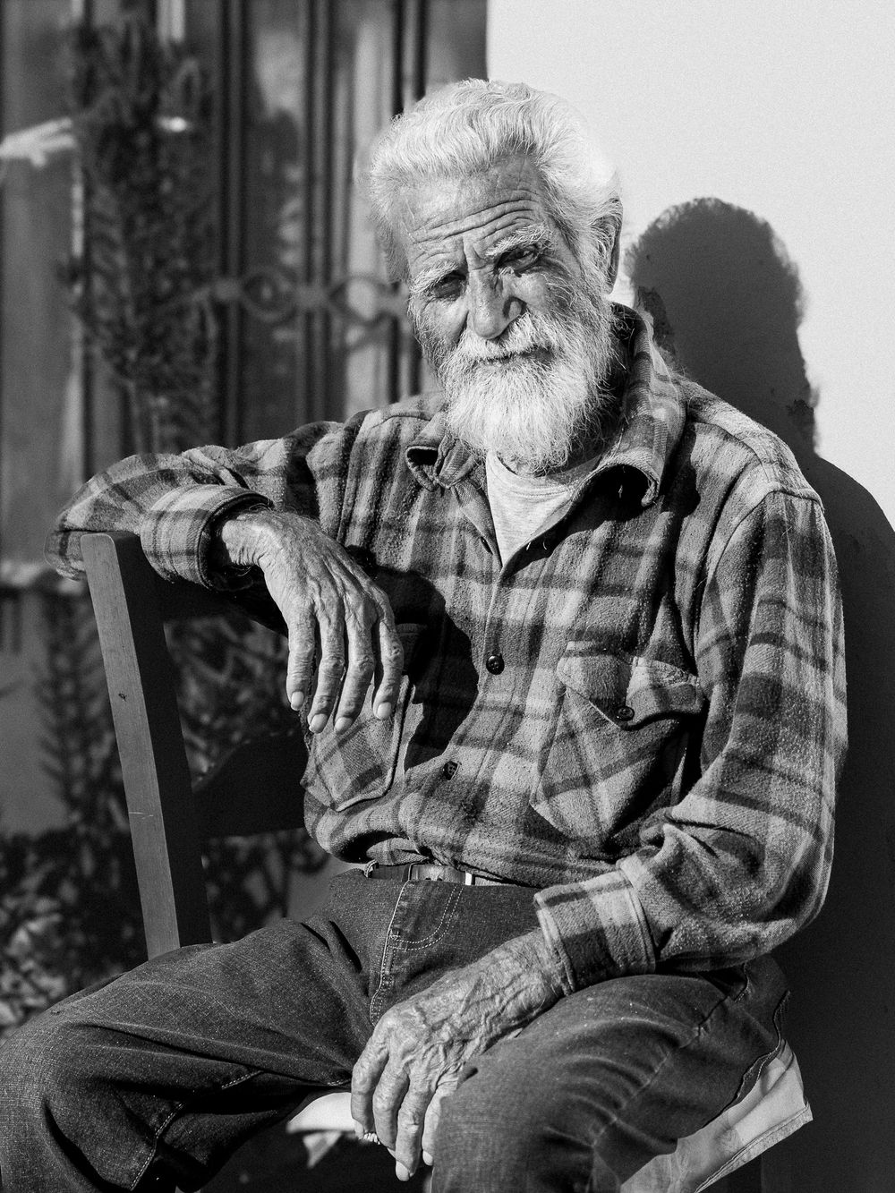 Black and white portrait of an elderly man sitting outdoors in natural light.