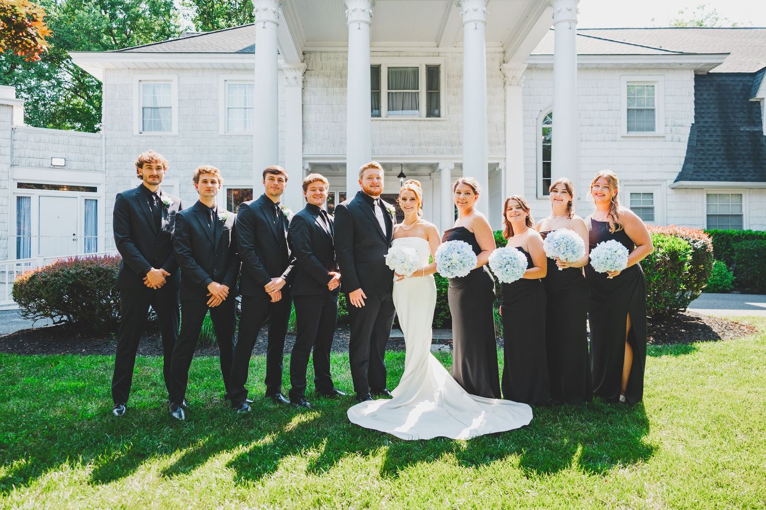 Wedding party in formal black and white attire poses together on lawn in front of Overhills Mansion in Catosville, Maryland
