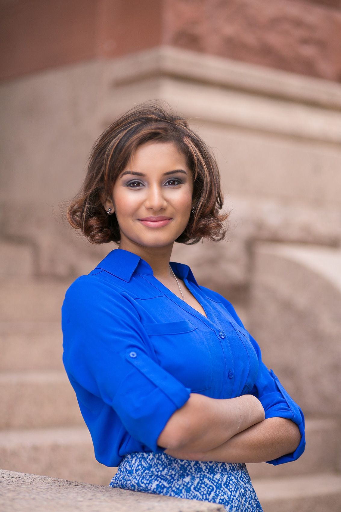 Professional headshot of someone in a bright blue blouse against a stone building background.