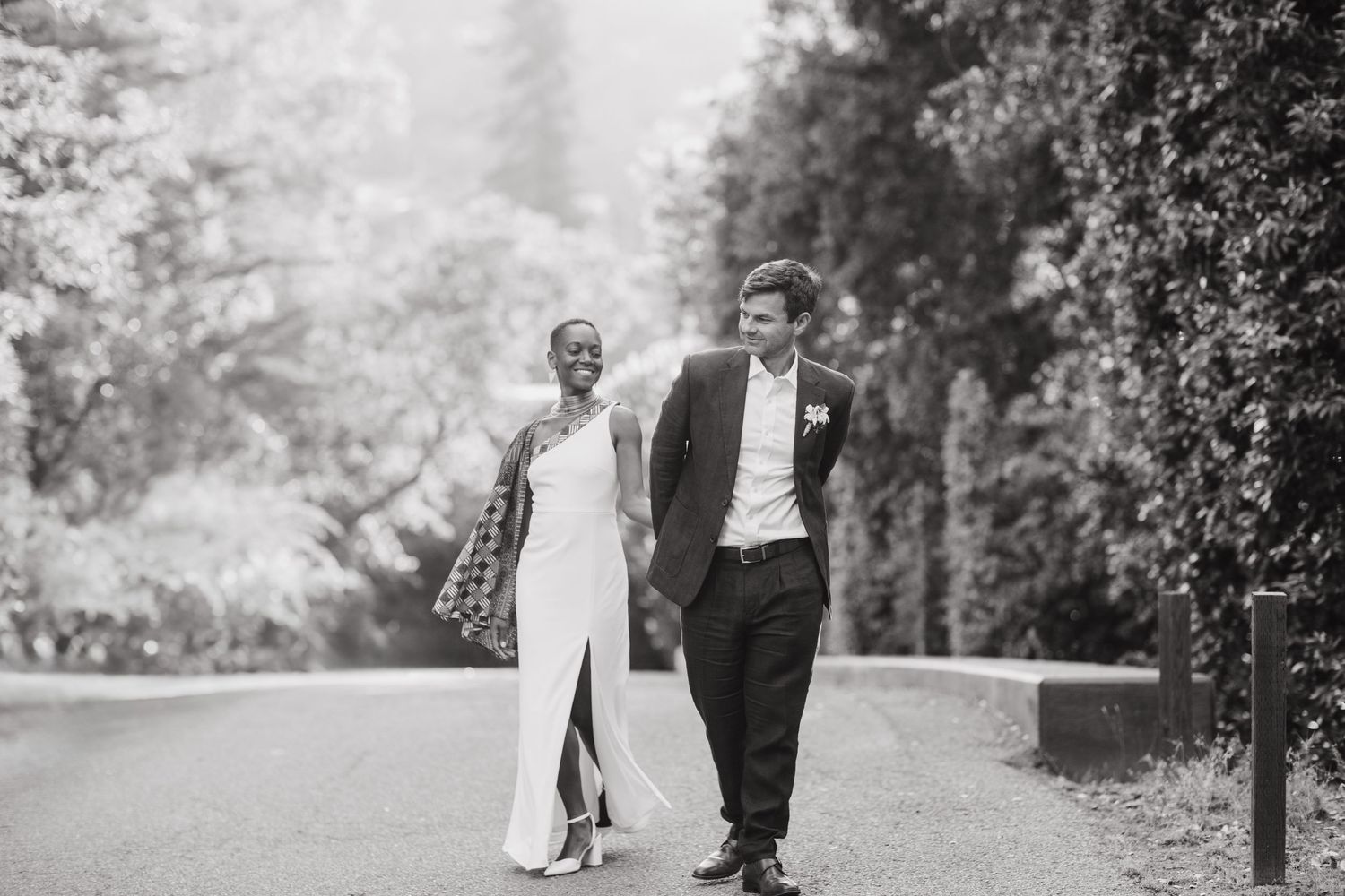 Black and white photo of the bride and groom walking hand in hand through the gardens at Geneva Terrace, Redlands University.