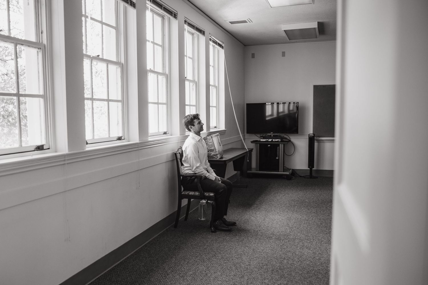 Black and white photo of the groom sitting alone in a quiet hallway before the ceremony at Geneva Terrace.