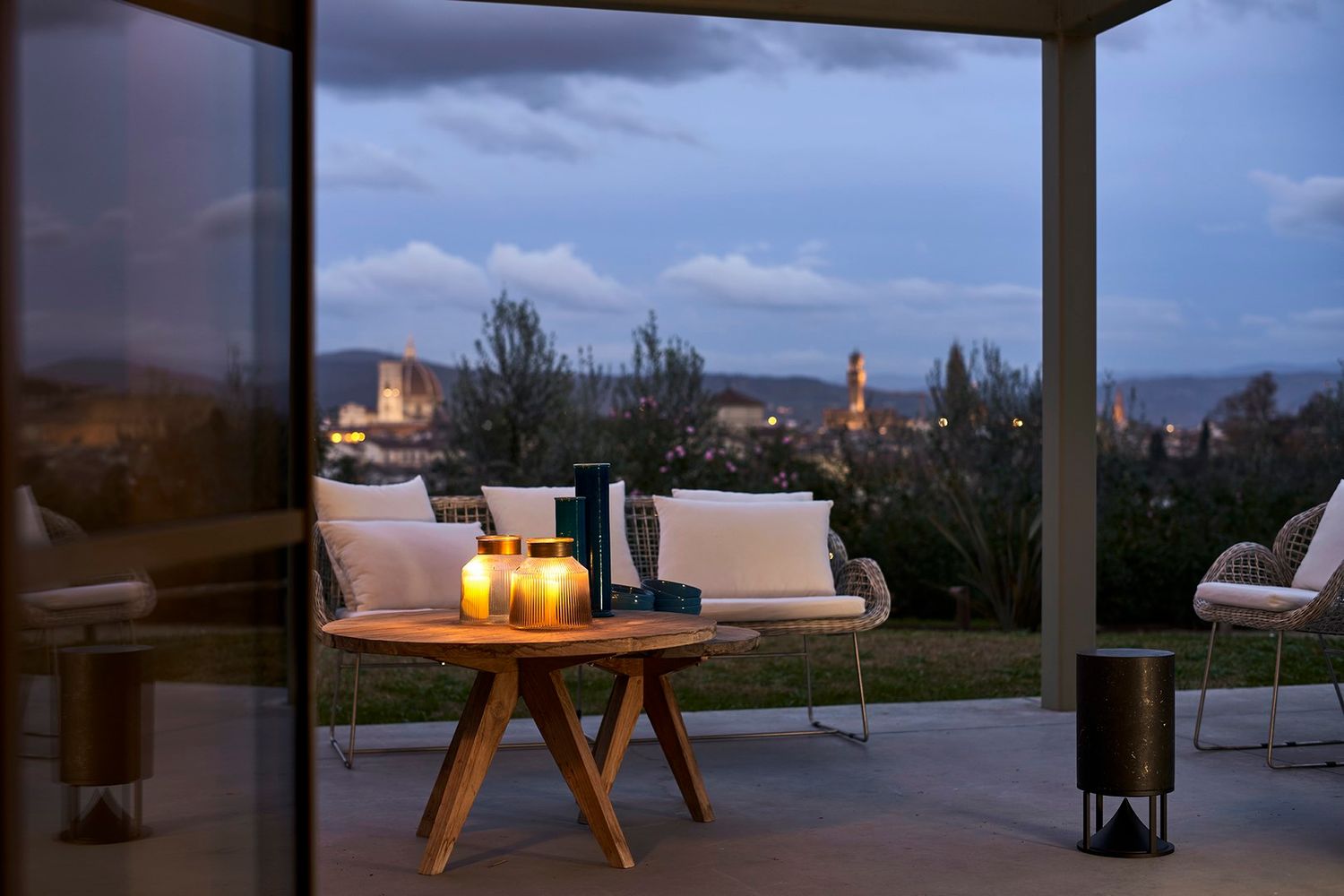 glass candle holders on wooden patio table at dusk with city lights twinkling in the background. Stone speaker by Architectura Sonora