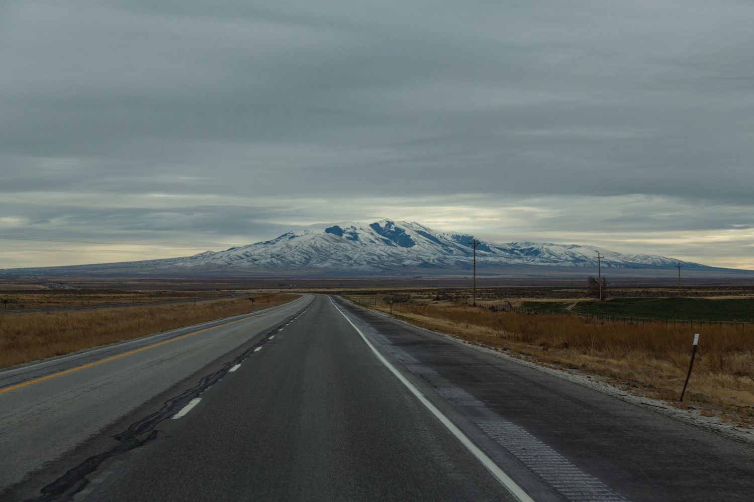 Long straight highway through desert plains with snow-capped mountains in the distance.