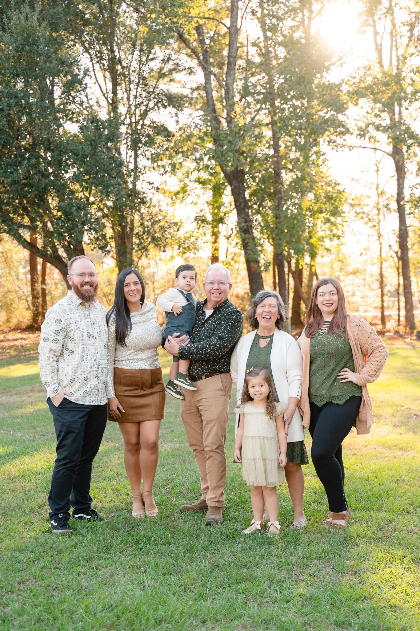 A group of people posing in a grassy field at sunset with golden sunlight filtering through autumn trees.