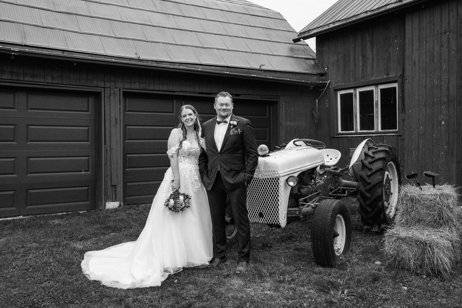 Bride and groom standing near a tractor- in black and white