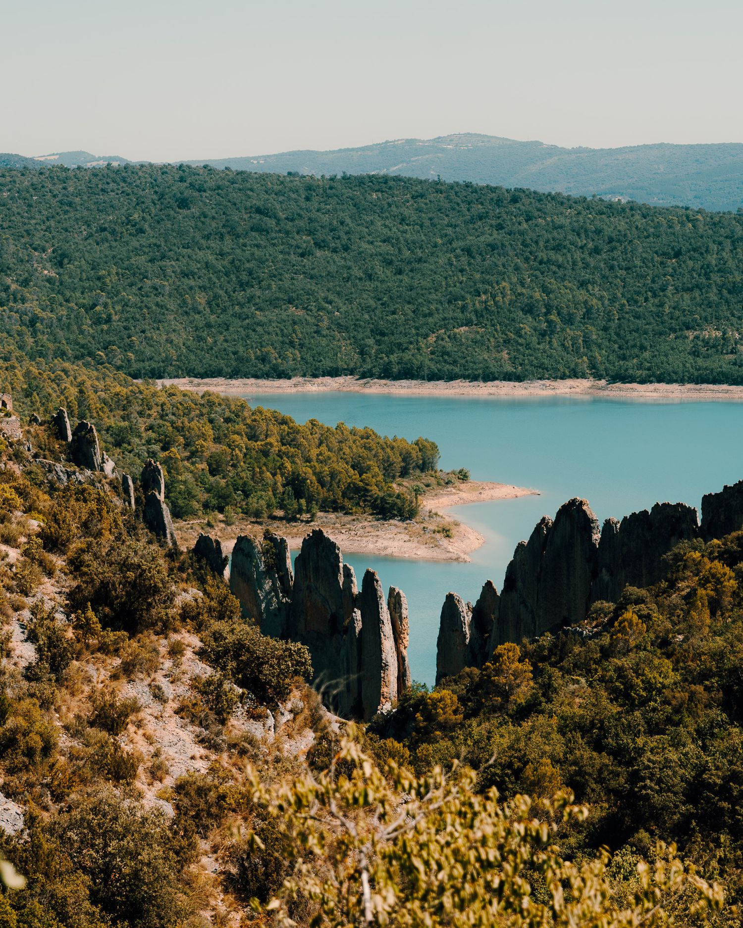 Turquoise lake surrounded by steep cliffs and dense forest in a mountainous landscape.