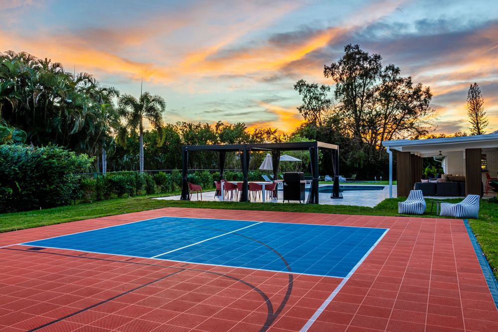 Outdoor tennis court with blue surface and red border against a dramatic sunset sky.