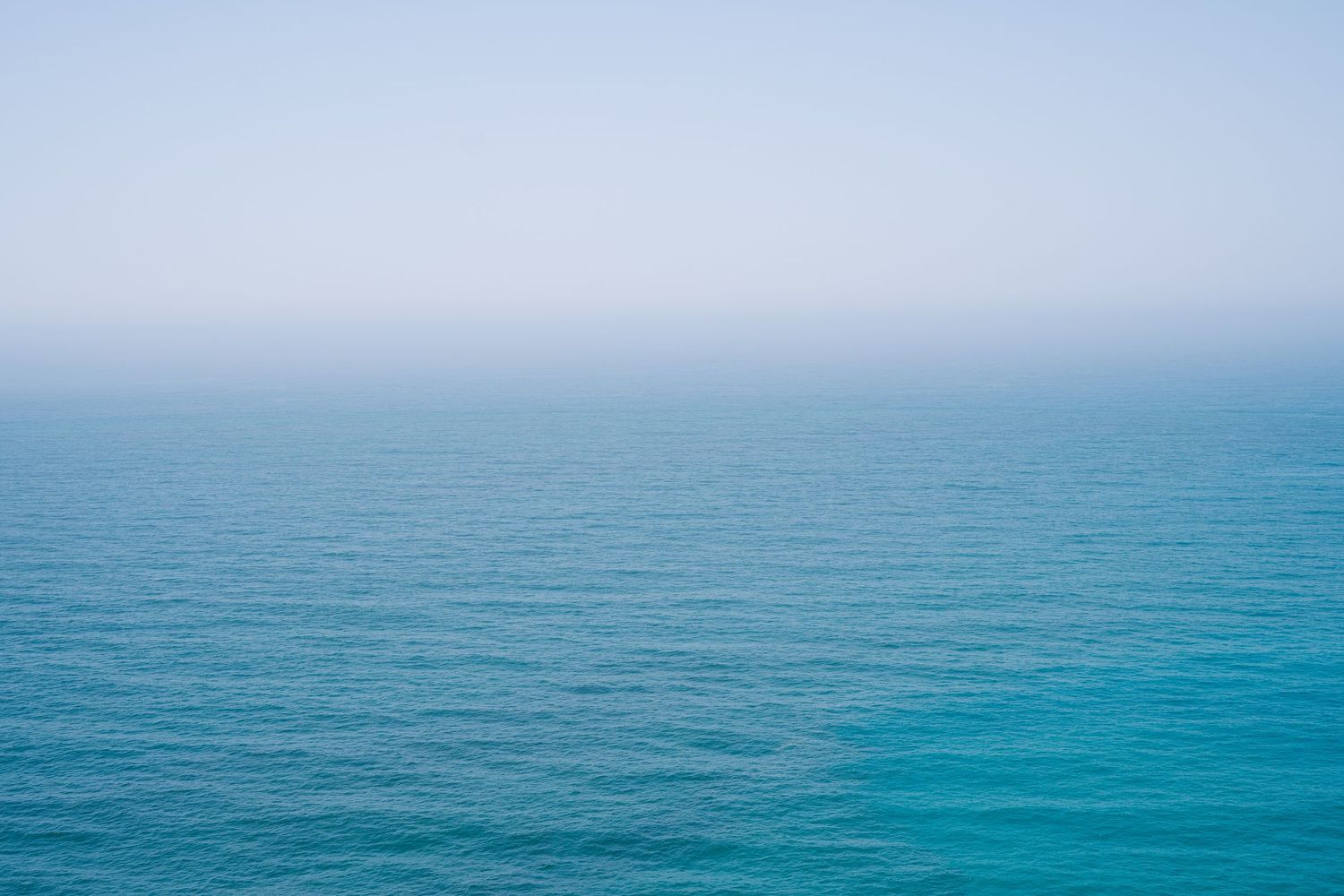 A tranquil ocean panorama with multiple panels showing turquoise waters stretching to the horizon under a misty sky.