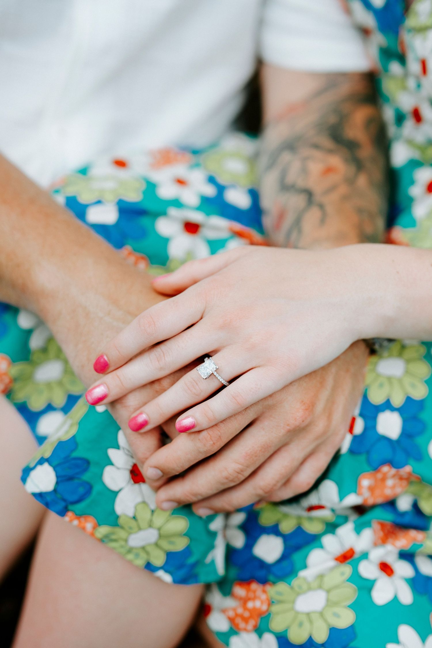 Close-up of hands showing off a new engagement ring against a floral blue dress pattern.