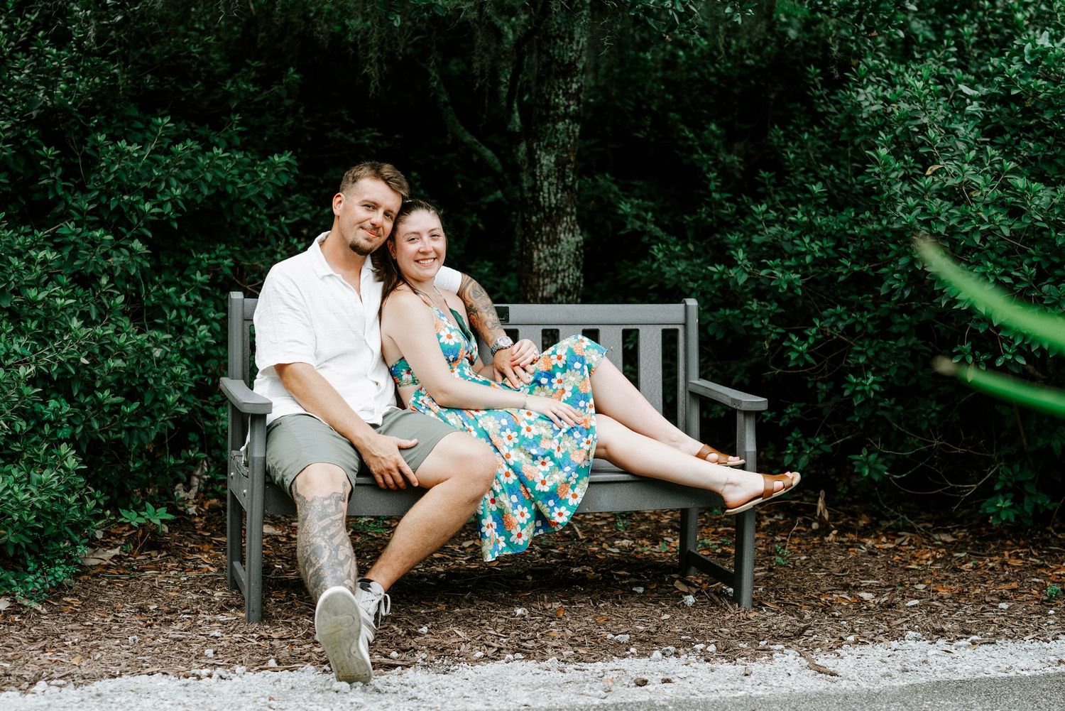 A couple sharing tender moments on a park bench surrounded by greenery.