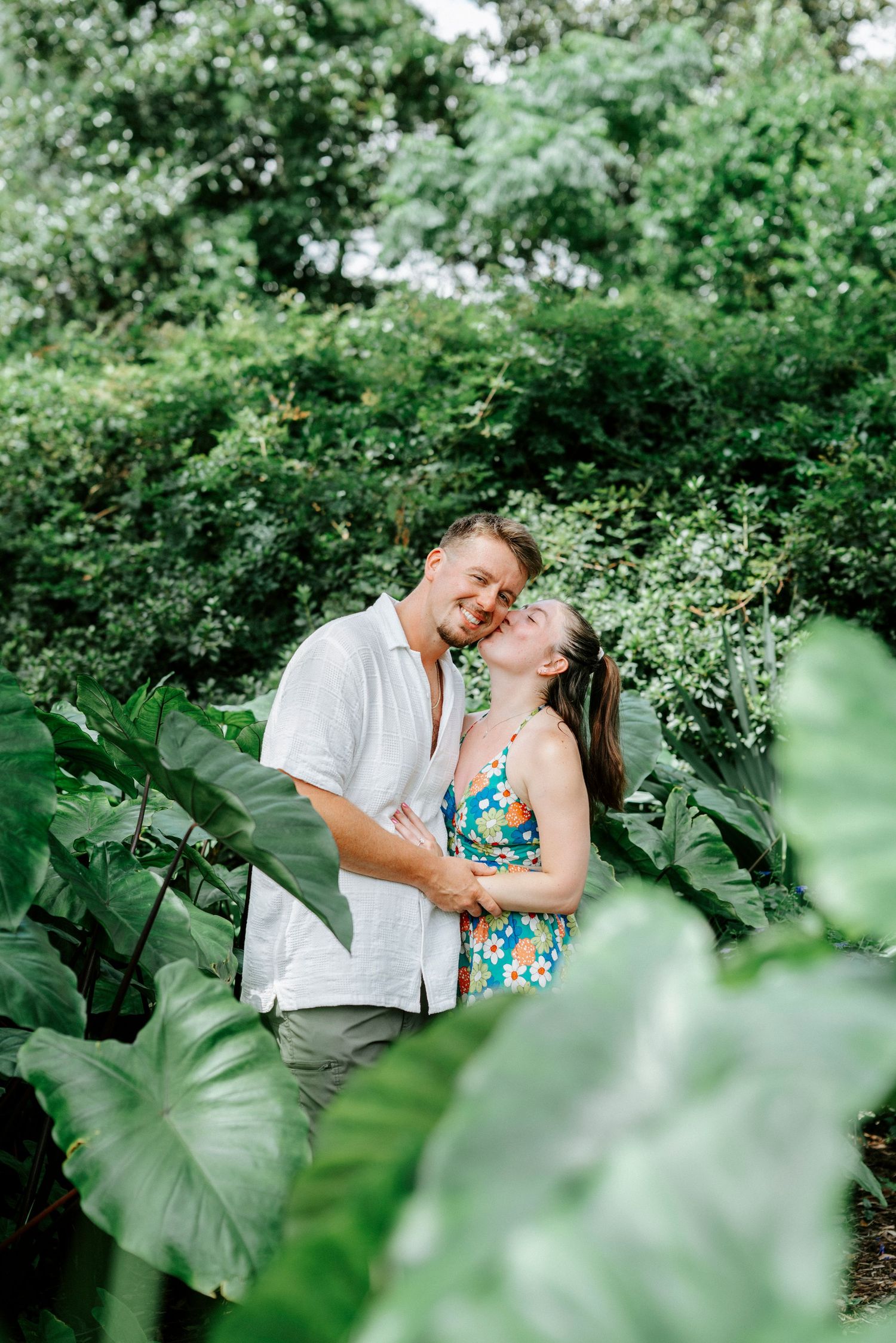 A couple embraces in a romantic garden setting surrounded by tropical foliage.