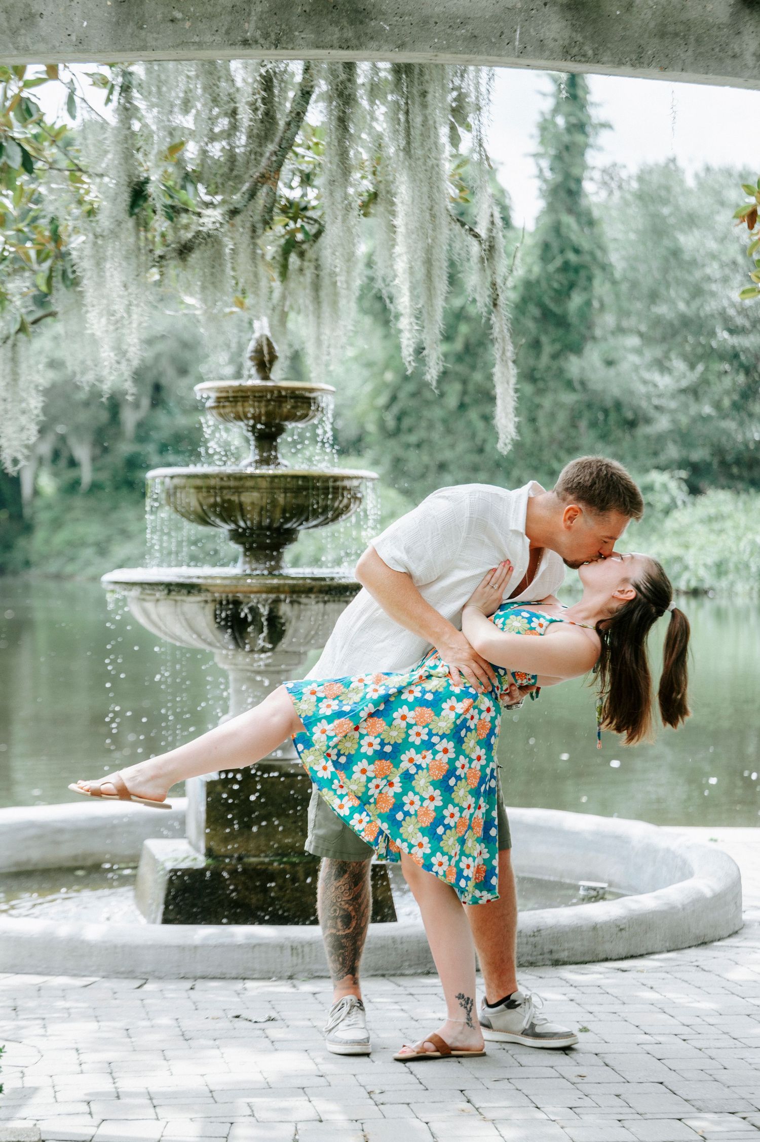 A couple performs a romantic dip pose near an ornate garden fountain.