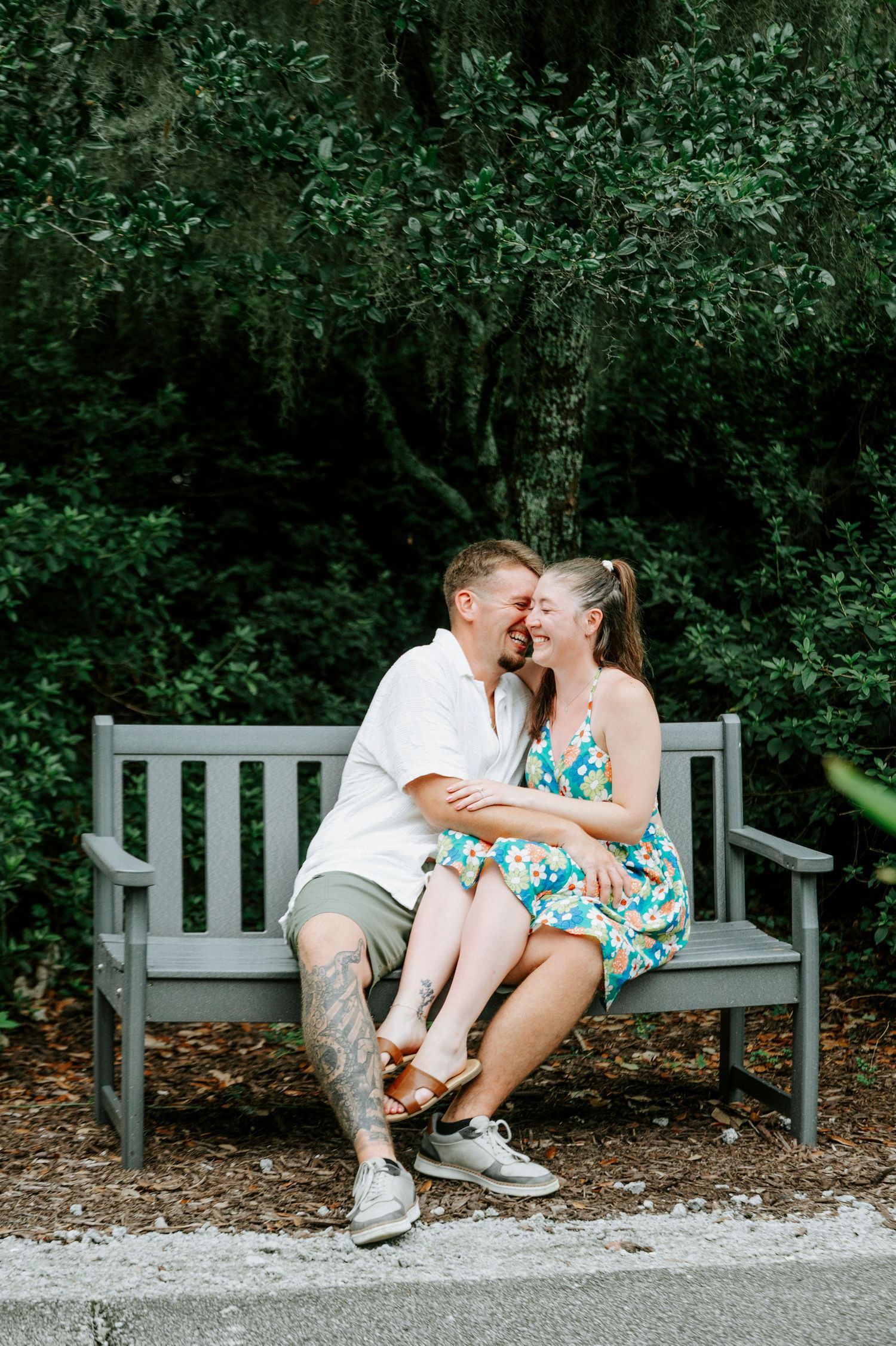 Couple sharing a playful moment while sitting on a bench among lush greenery.