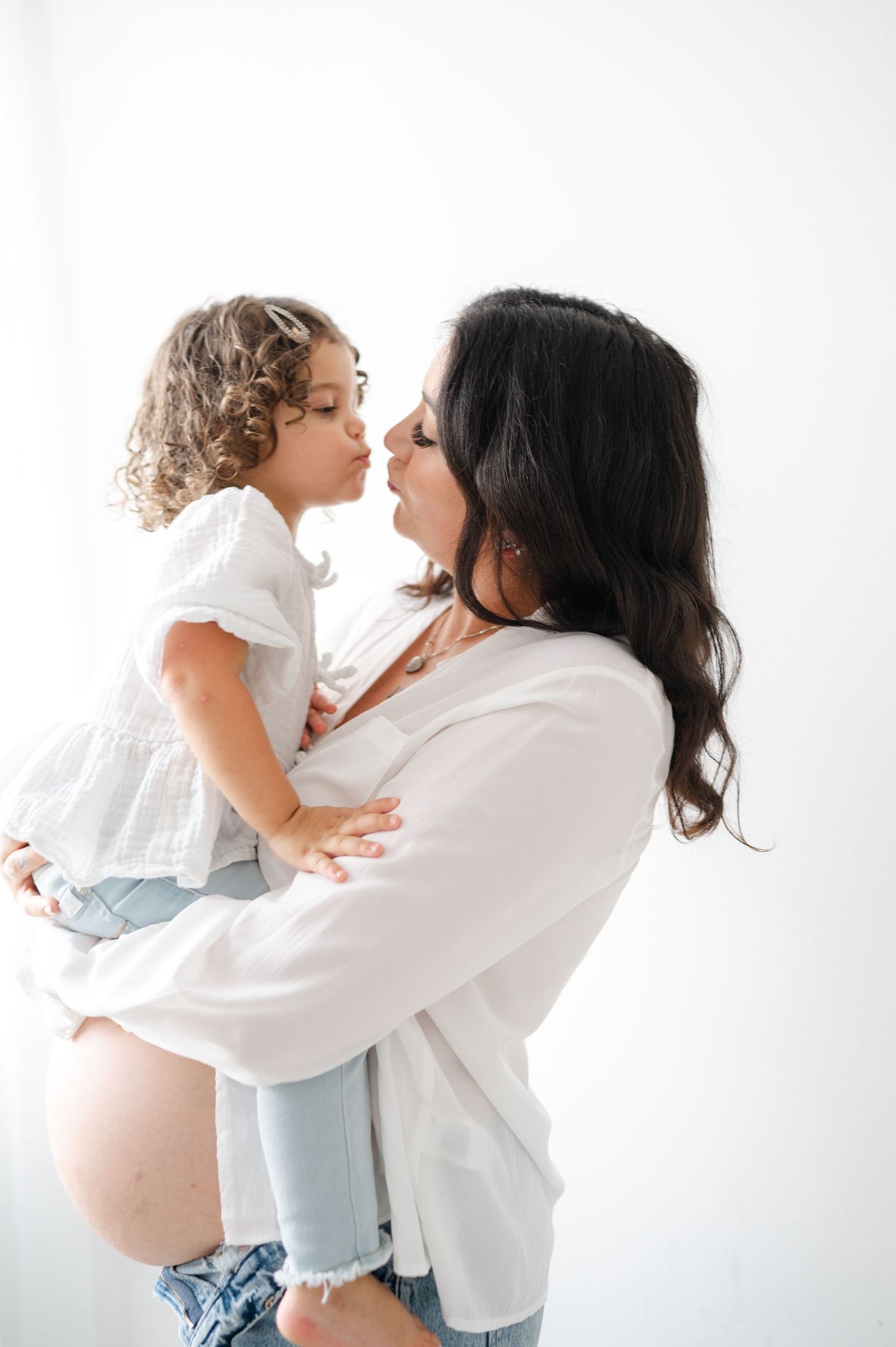 Sweet interaction between mother and child during a maternity photoshoot in white and denim.