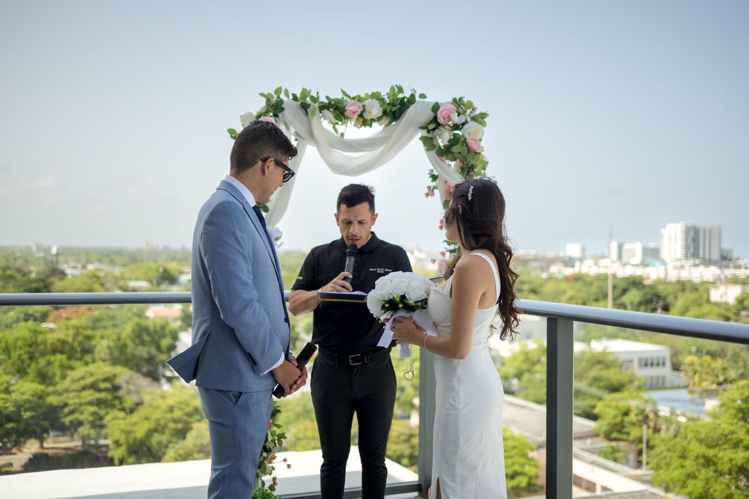 An intimate rooftop wedding ceremony takes place with beautiful green trees and city skyline in the background.