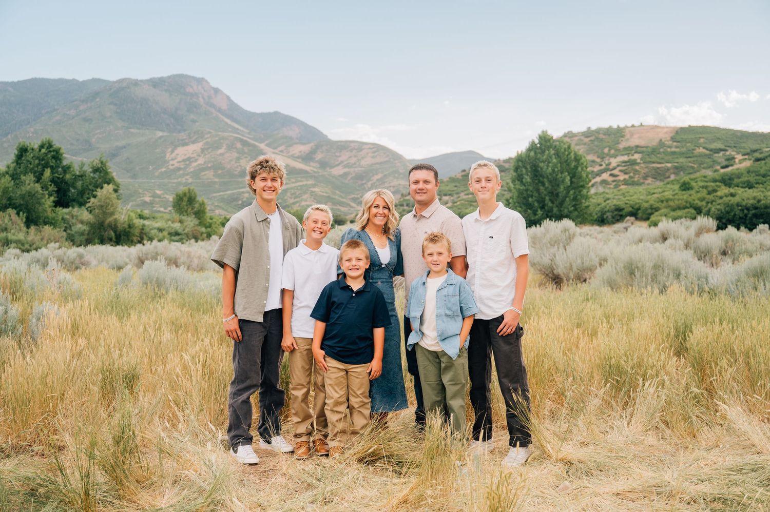 A sequence of scenic outdoor family photographs taken in a grassy field with mountains in the background.