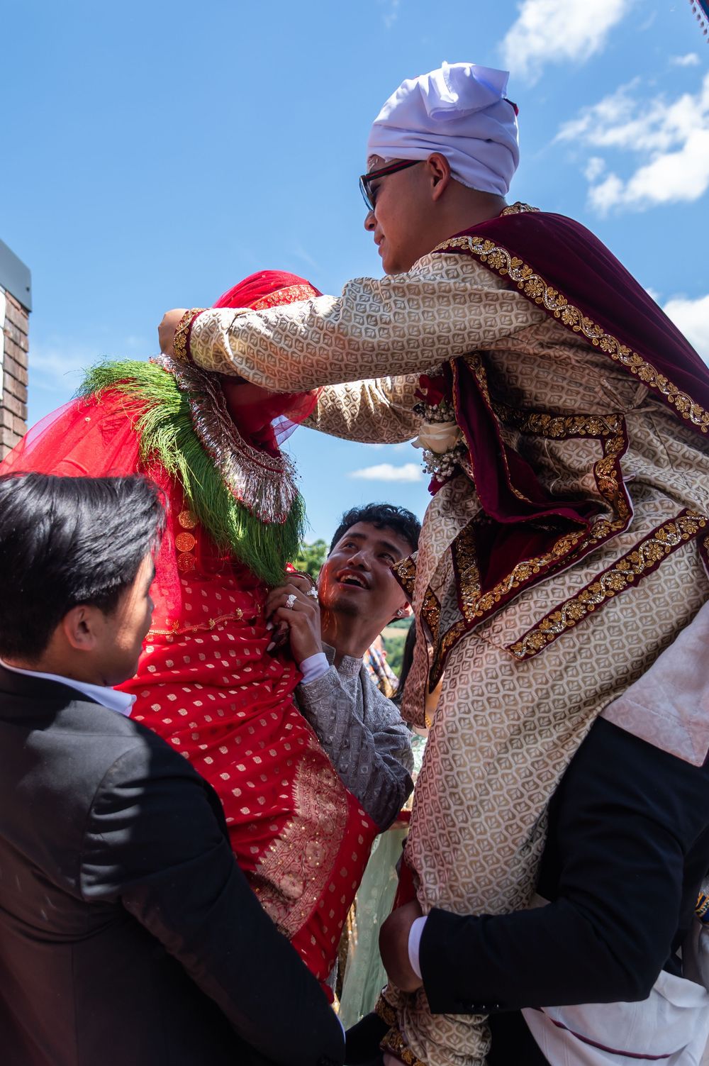 A couple in traditional South Asian wedding attire embracing during an outdoor ceremony.