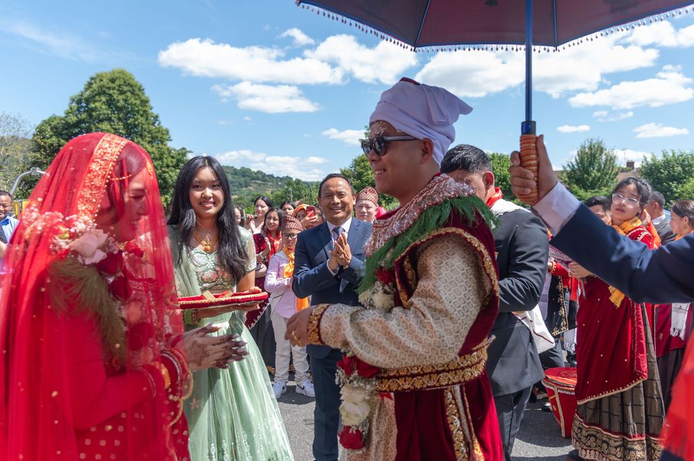 Outdoor Indian wedding ceremony under a red umbrella with guests gathering in summer weather.