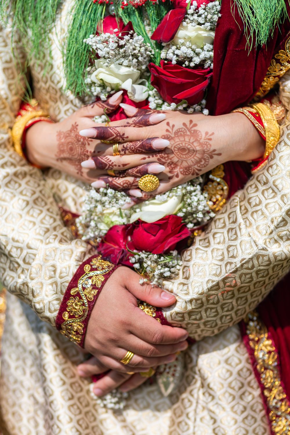 Detailed shot of hands with henna designs holding traditional wedding flowers and decorations.