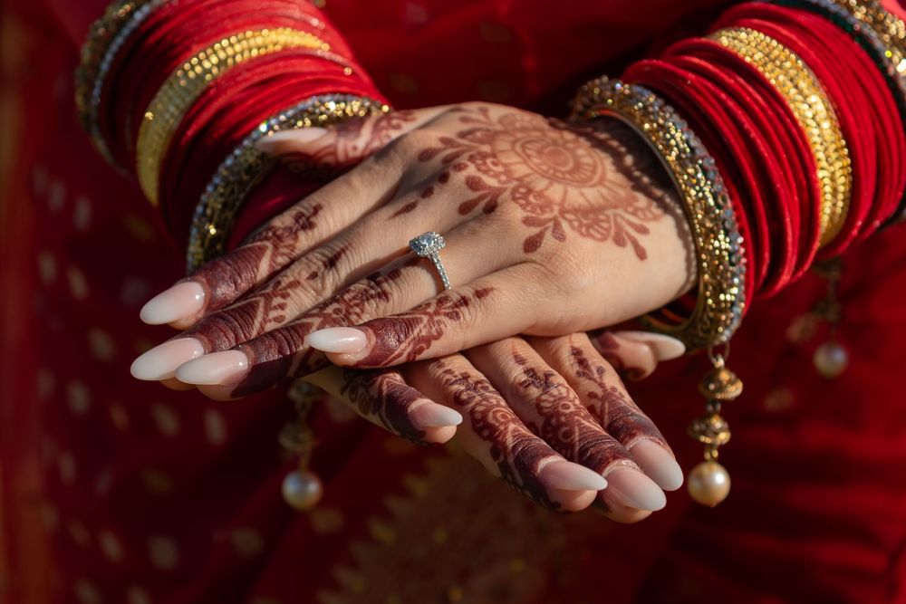 Close-up of intricate henna designs on hands with traditional red and gold bridal attire.