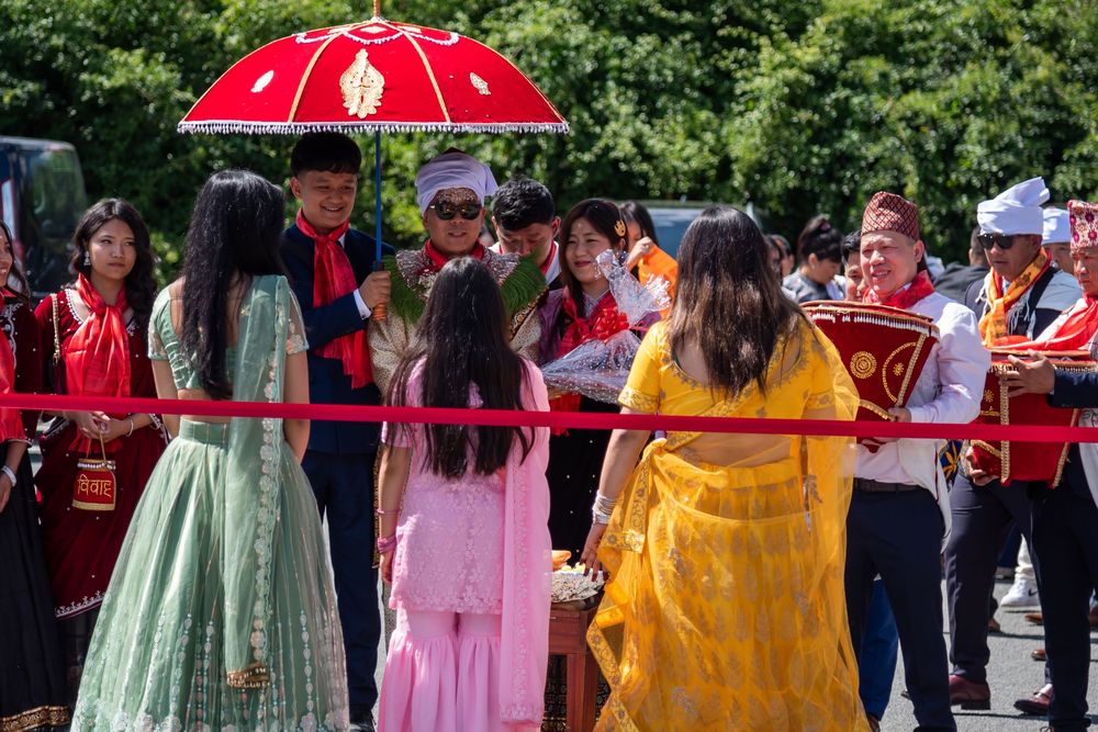 Large group celebrating an Indian wedding ceremony outdoors with colorful traditional attire and red parasol.