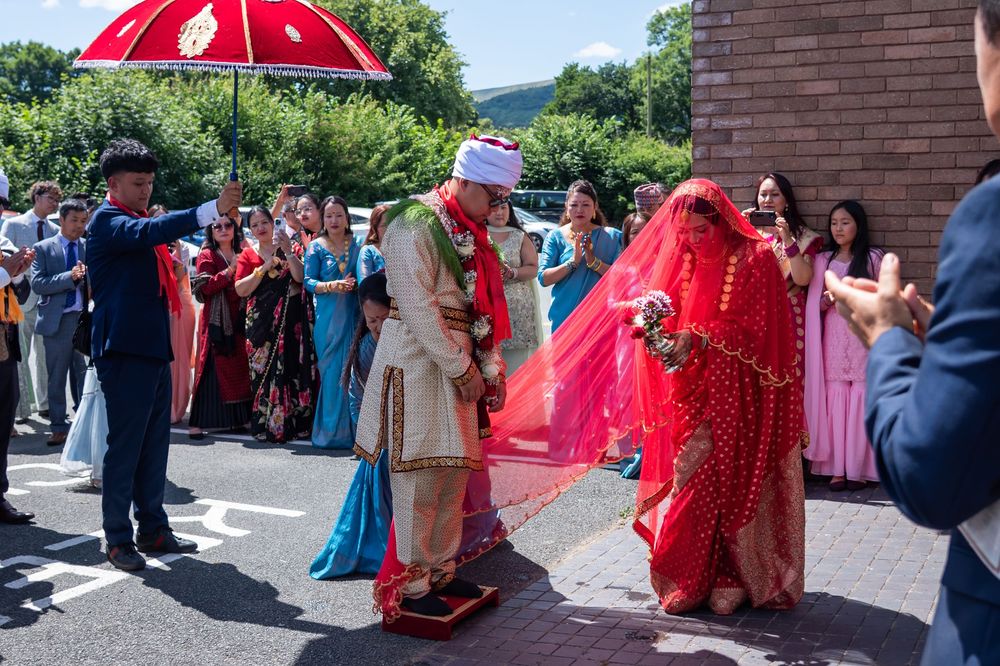 Traditional Indian wedding procession outdoors with bright red umbrella and decorative cultural attire.
