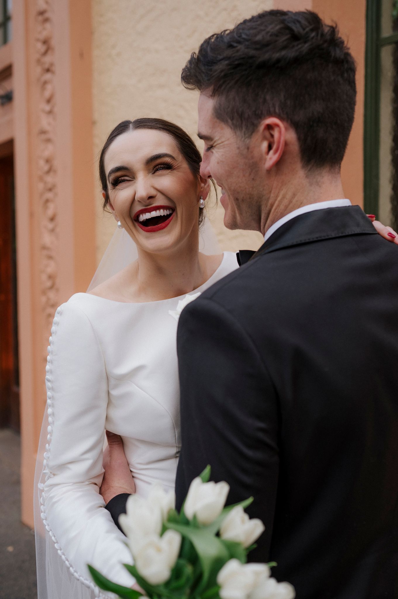 Candid wedding moments captured against salmon-colored conservatory building.